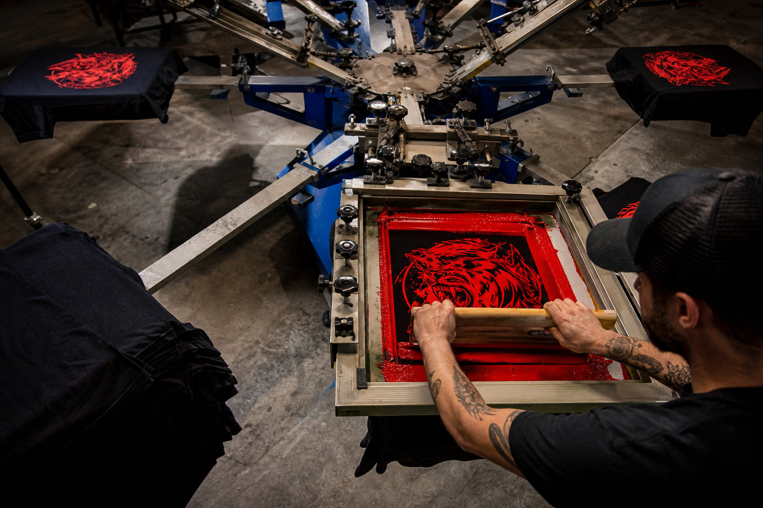 Screen printing press in action with red ink being pulled across a screen — The Printing Needle Garden Grove