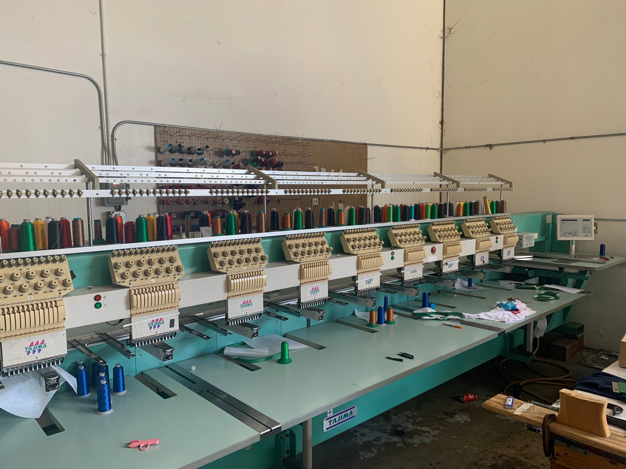 Embroidery machine setup in a workshop with multiple embroidery units and spools of thread.