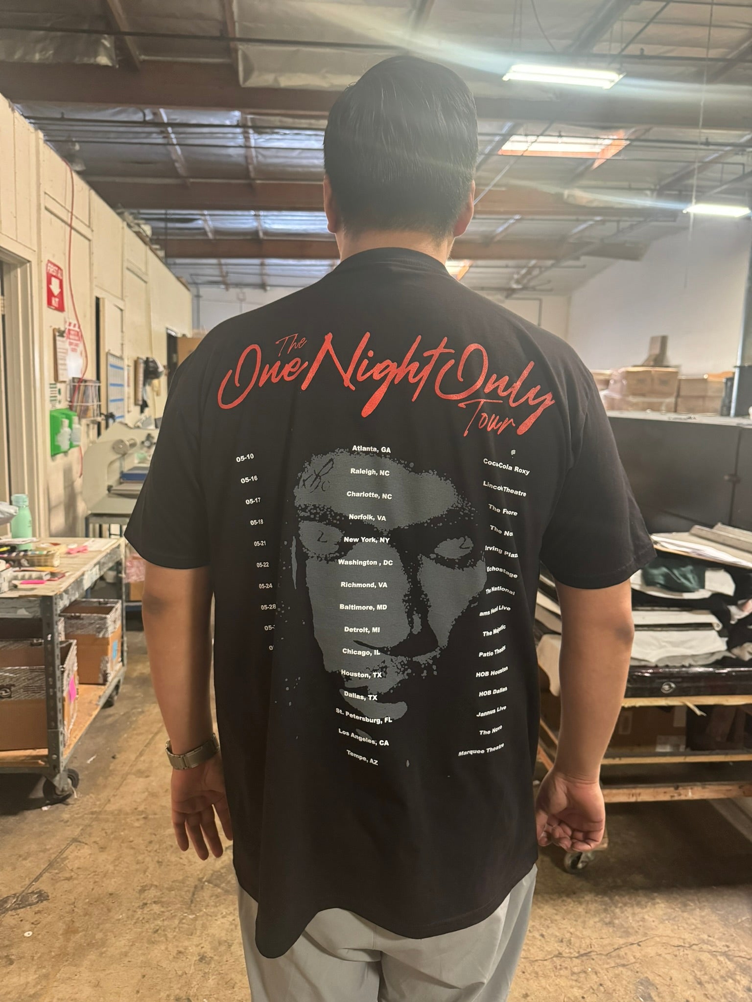 Person wearing a black t-shirt with 'One Night Only' design in a warehouse setting