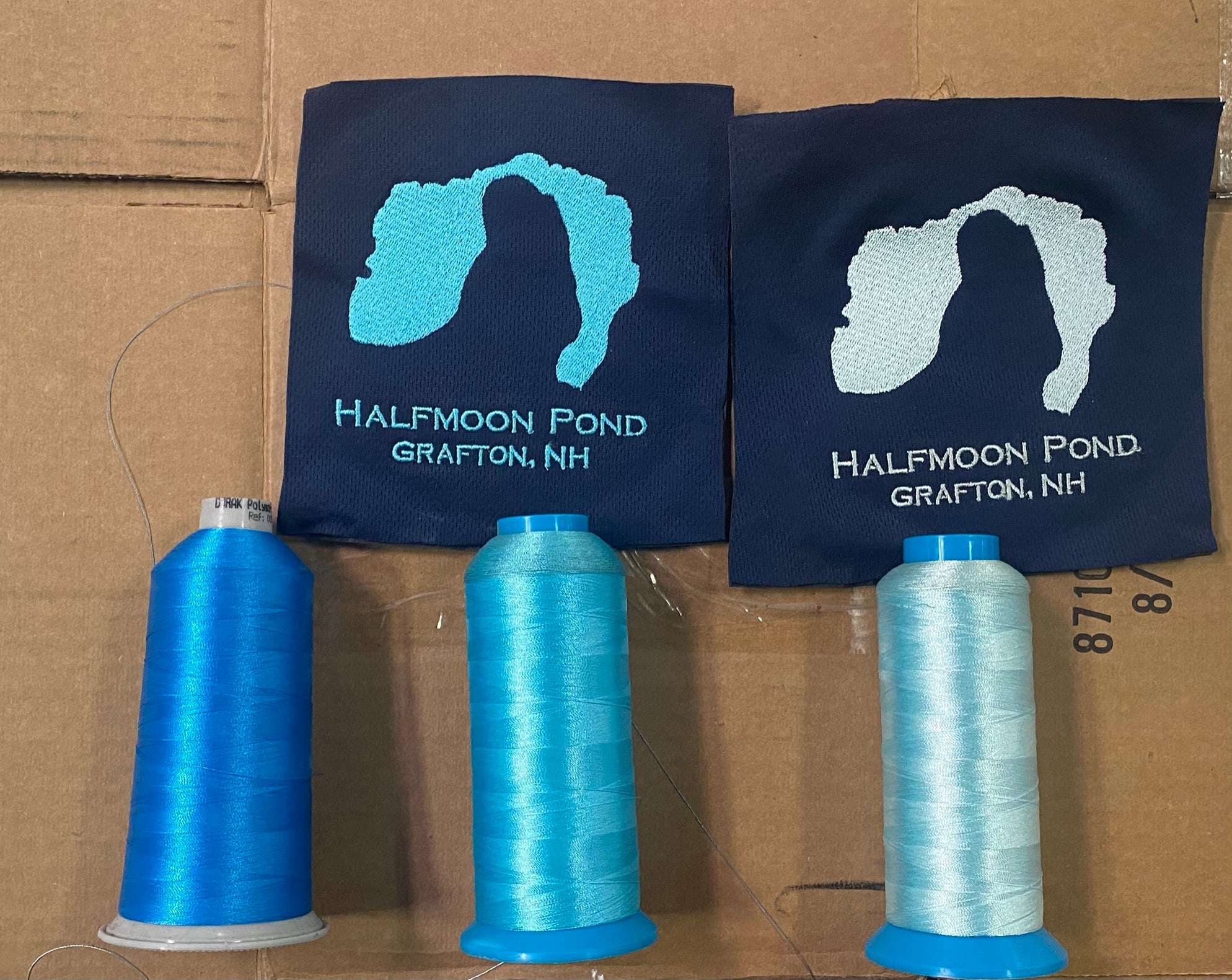 Two blue bags with a logo and text, accompanied by spools of blue thread on a cardboard background.